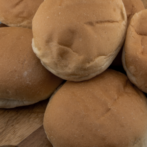 Close-up of six classic white bread buns arranged on a wooden board.